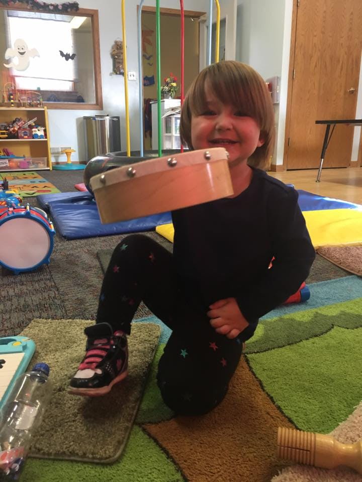 Child kneeling on a rug holding a tambourine