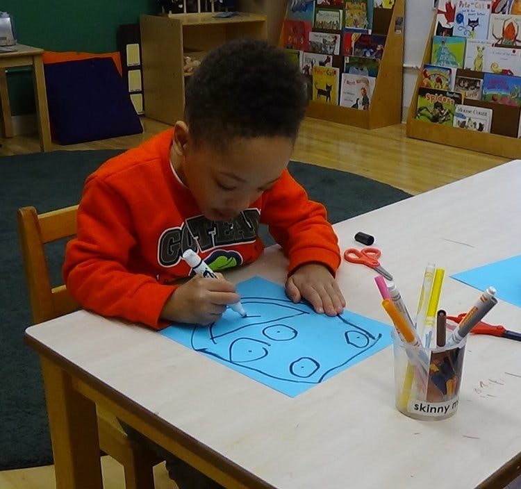Child drawing on blue paper with a marker at a table