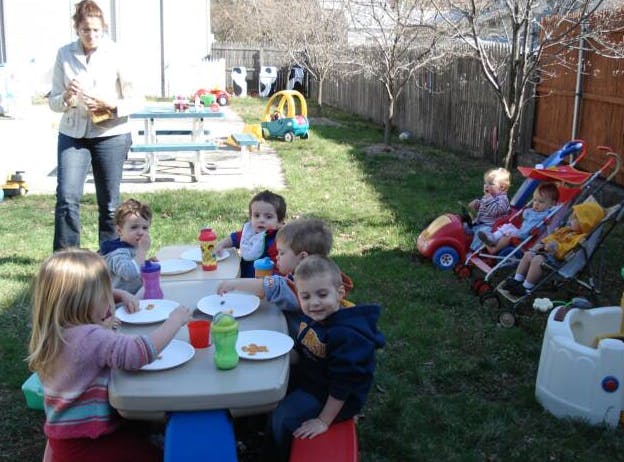 Adult standing near children seated at a table outdoors
