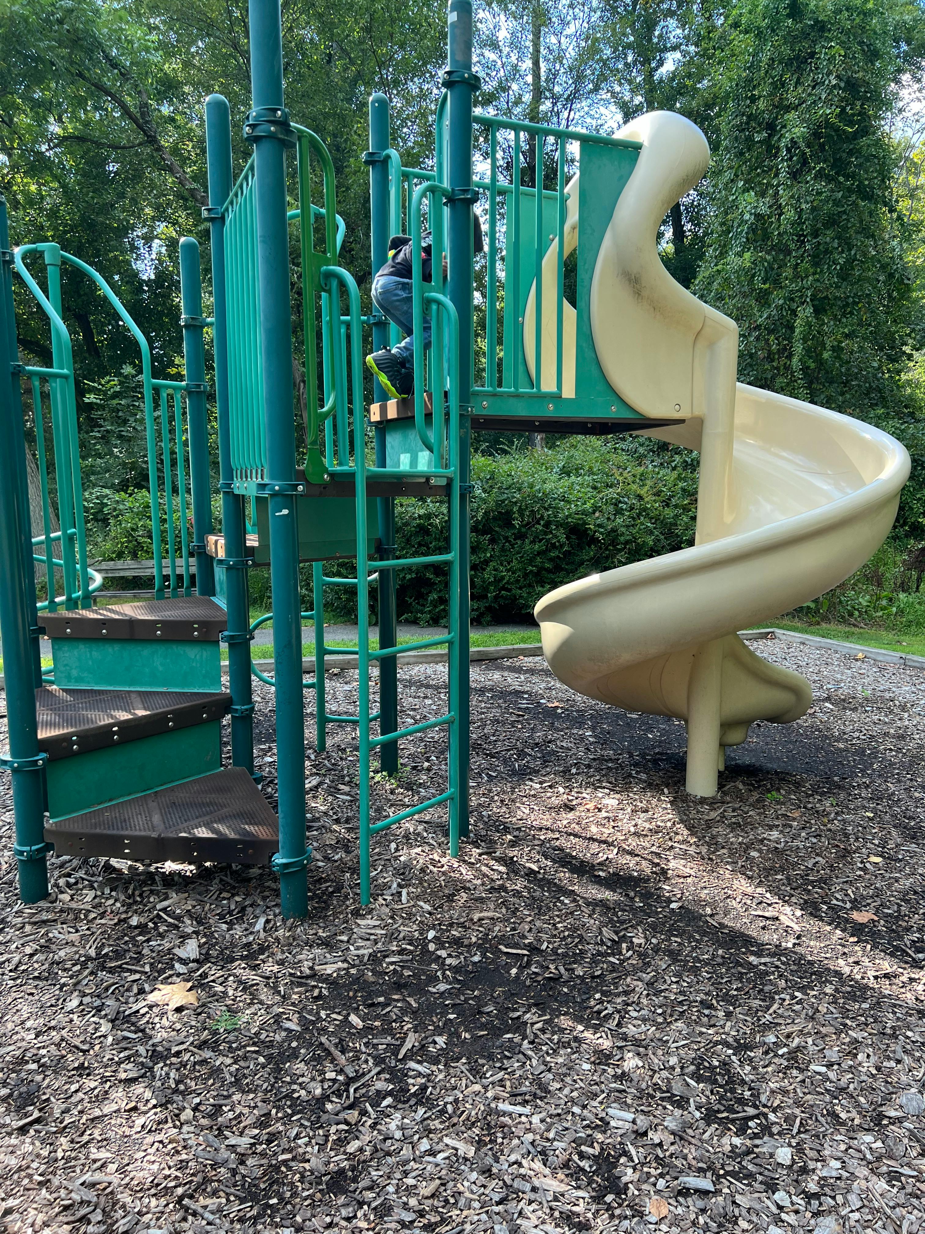 Child climbing on a green playground structure with a spiral slide