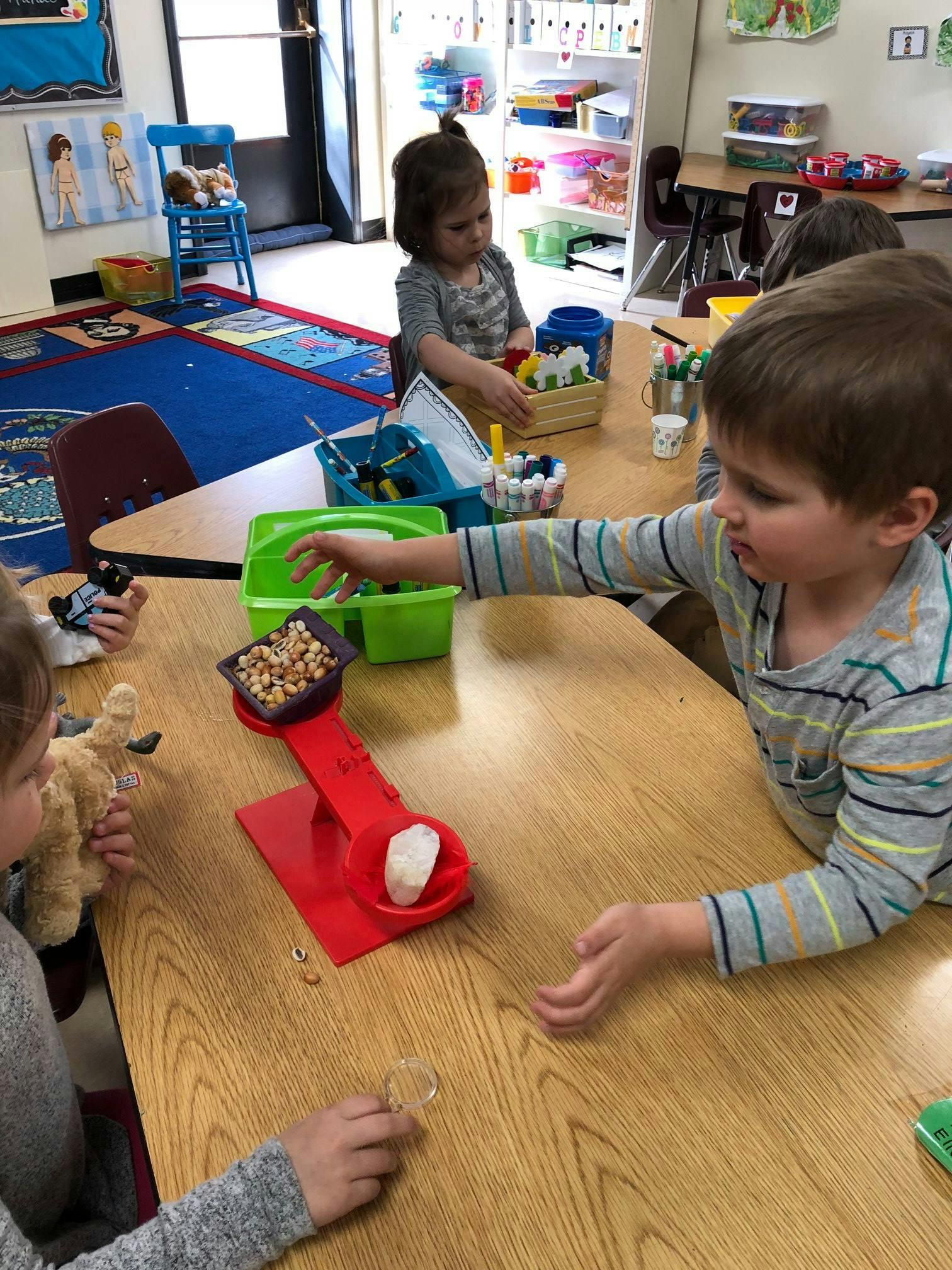 Children playing with a scale and other items at a table