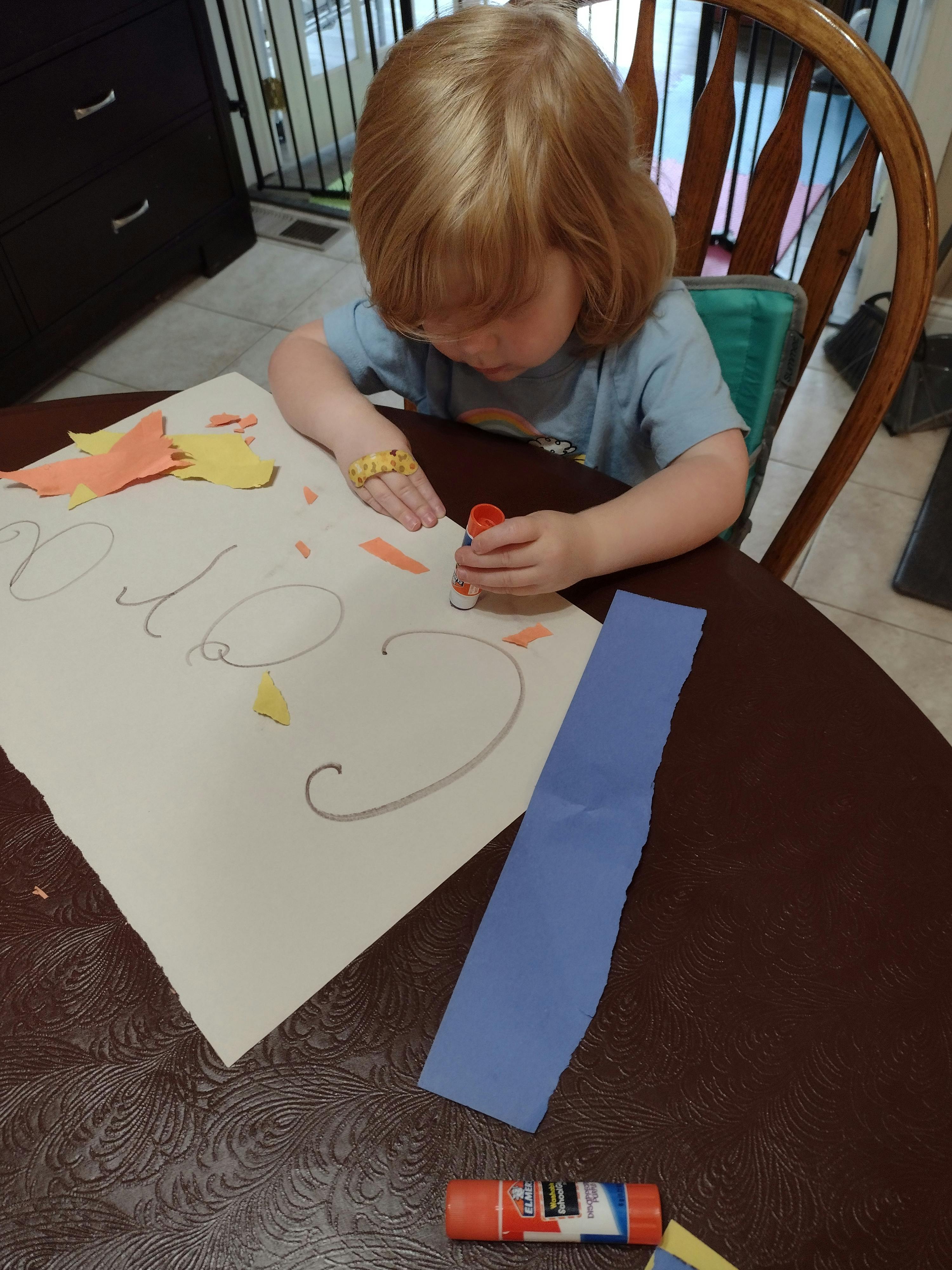 Child gluing paper cutouts onto a large sheet of paper