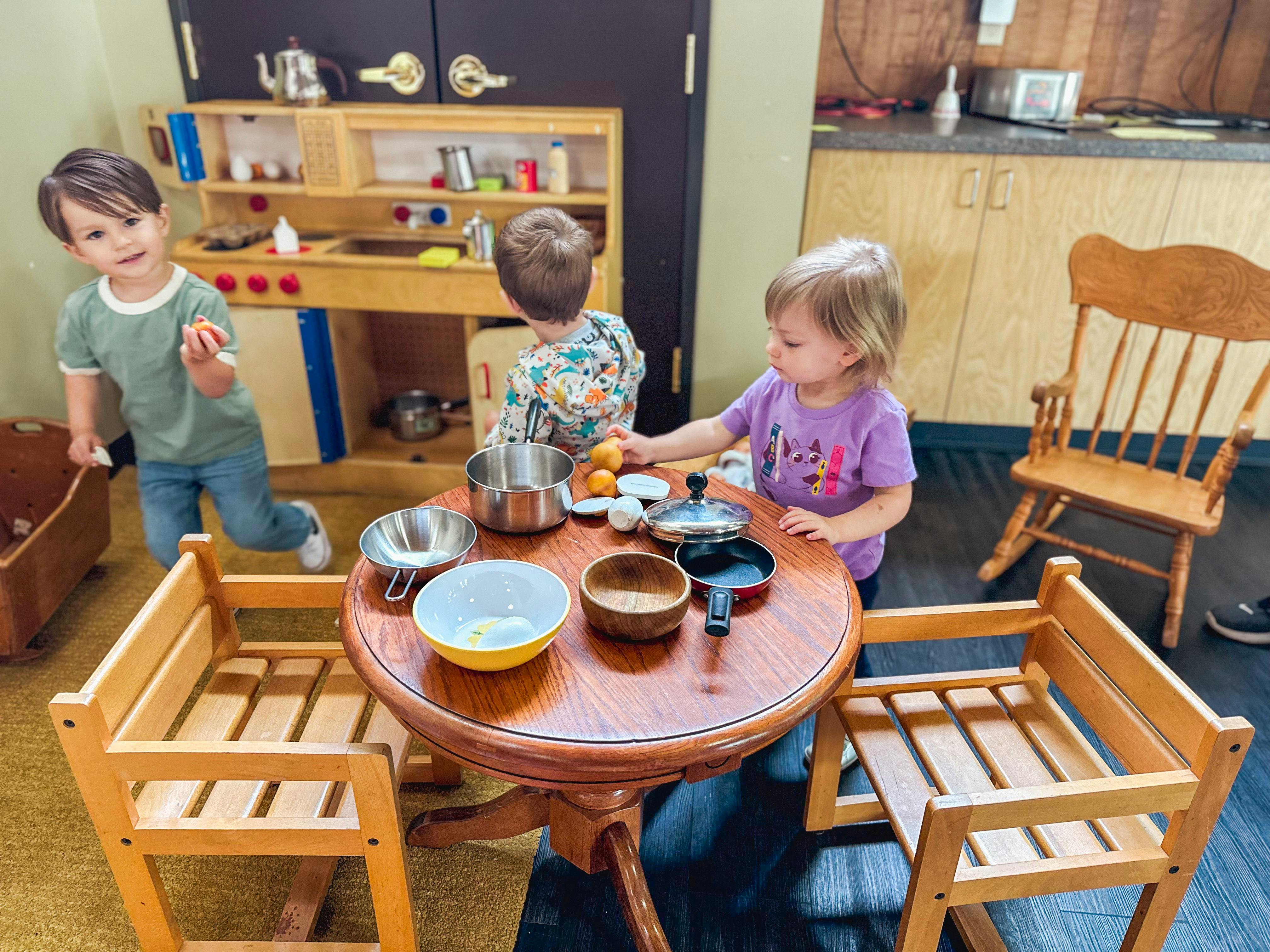 Three children playing with toy kitchenware at a table