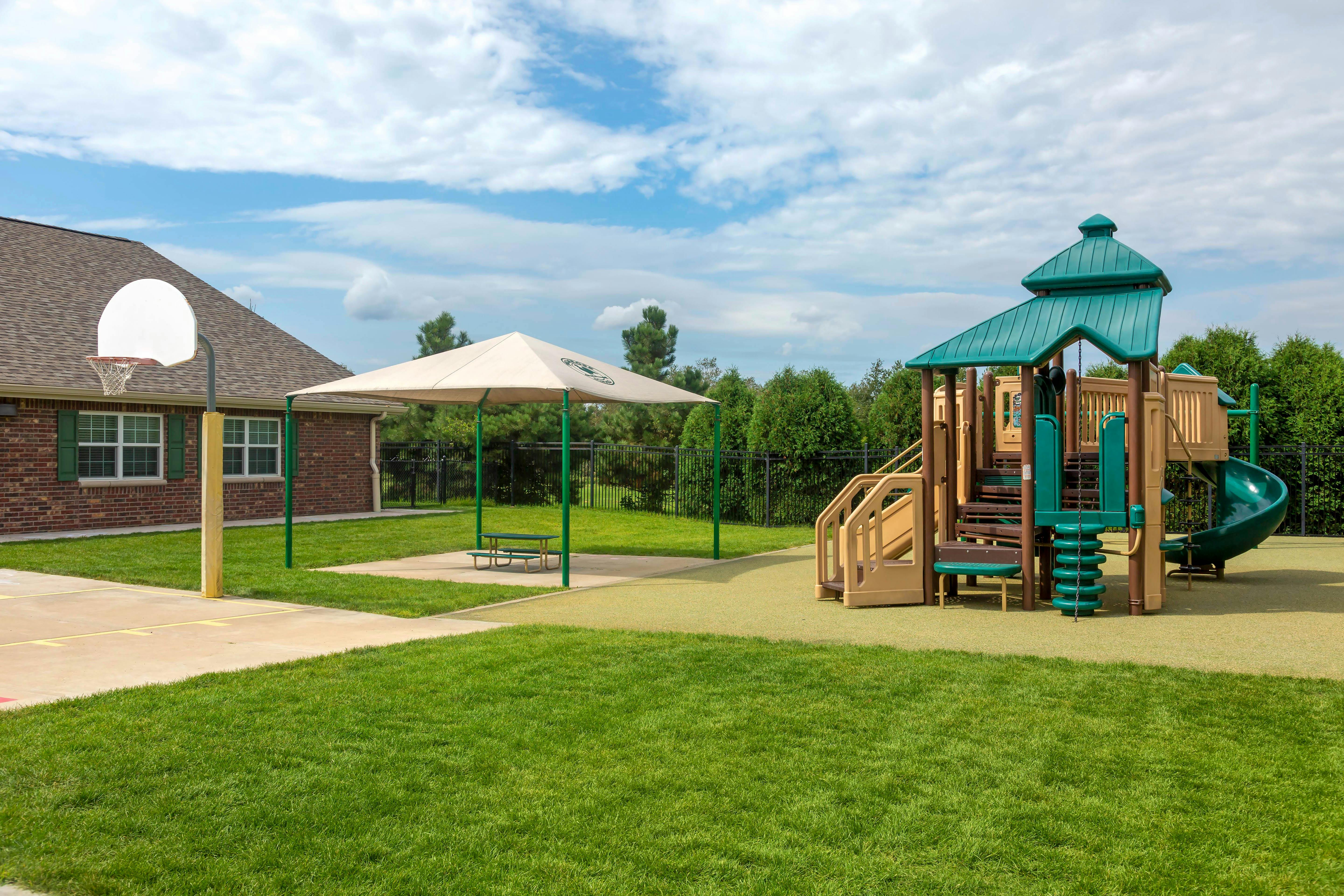 Basketball hoop, covered picnic table, and playground in a grassy area