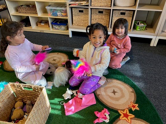 Three children playing on a rug in a classroom