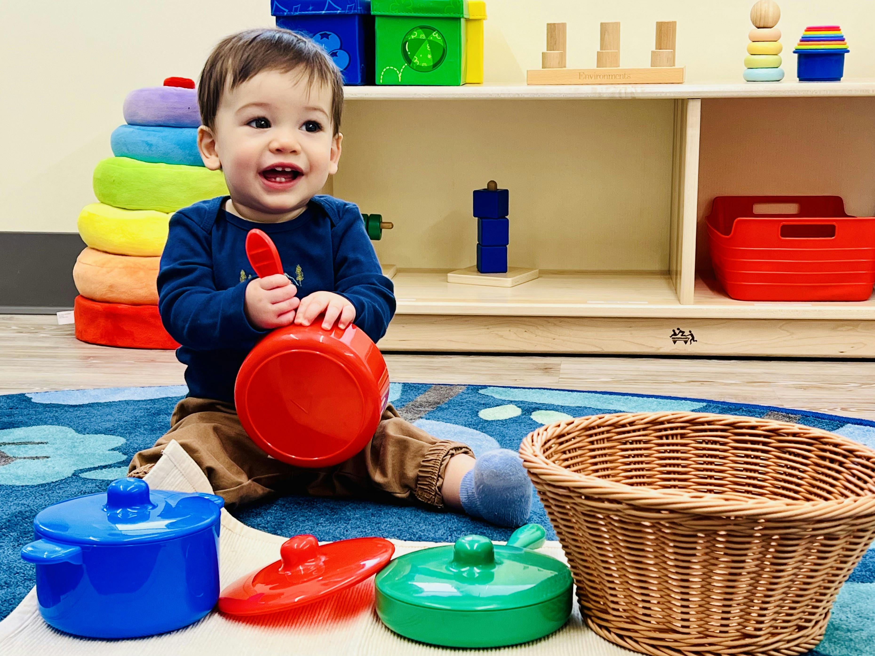 Smiling child playing with a red toy pot and spoon in a classroom