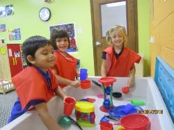 Three children playing with toys in a water table