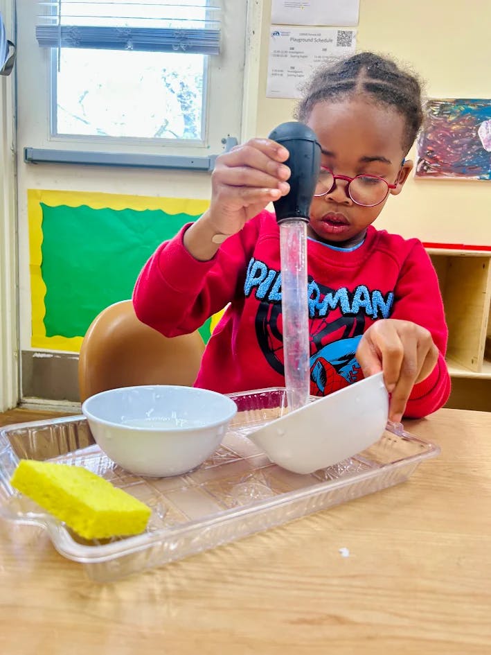 Child in a red shirt playing with a pipette and bowls in a classroom