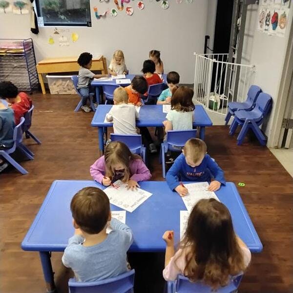 Children sitting at blue tables and writing in a classroom