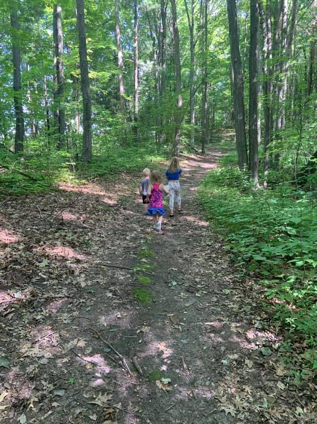 Three children walking on a dirt path through a forest
