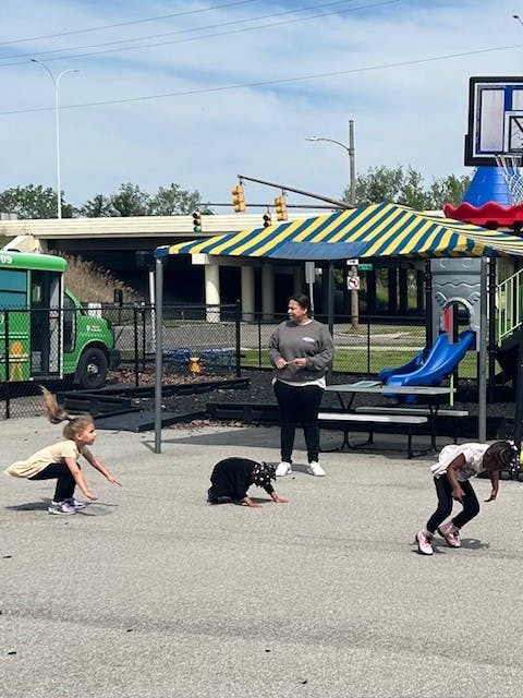 Adult and three children playing on a paved area near a playground