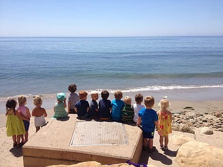 Children sitting and standing on a beach looking at the ocean