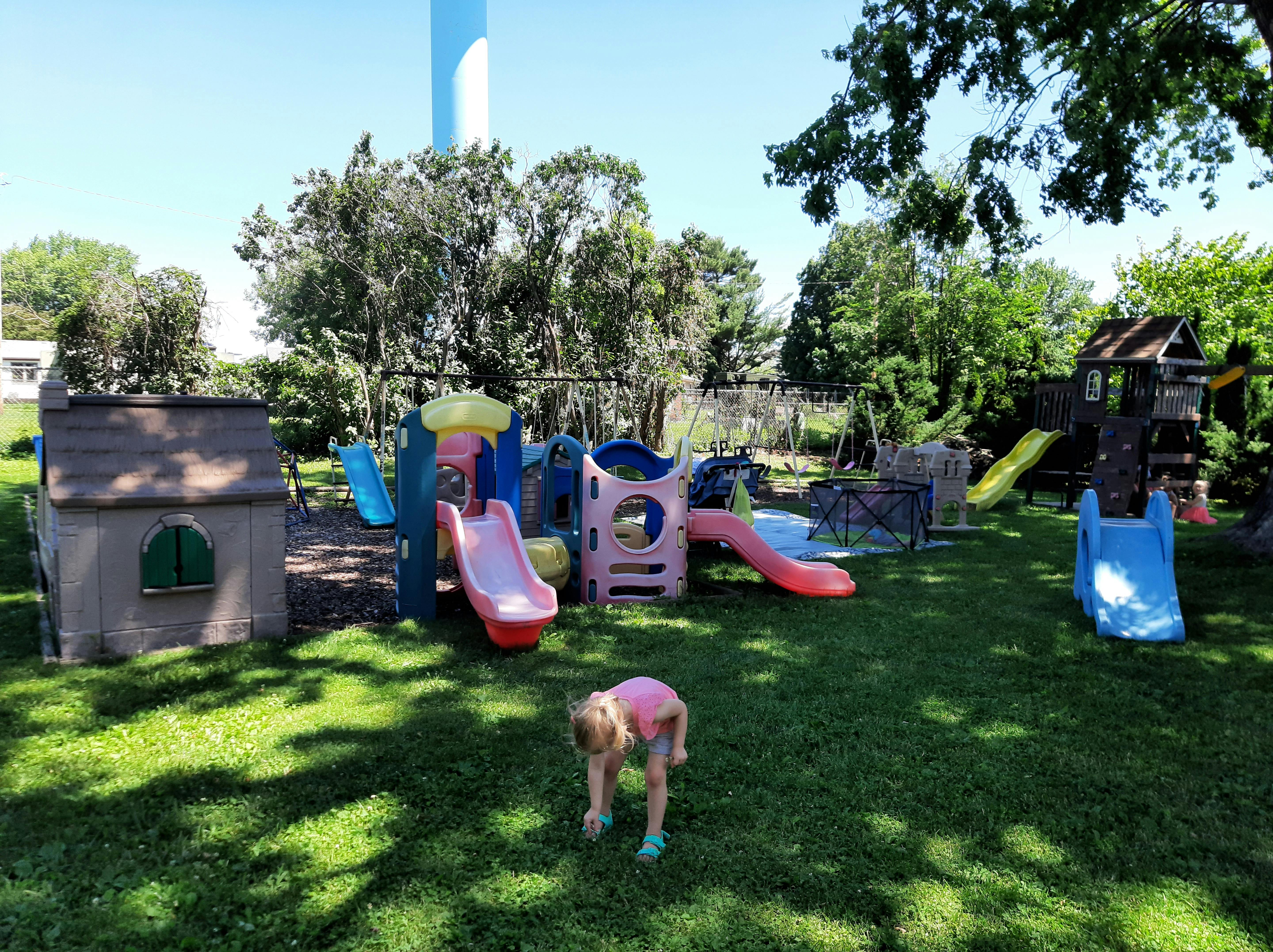 Child bending over on a grassy playground with slides and playhouses