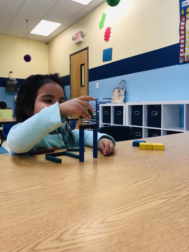 Child playing with building blocks at a table in a classroom