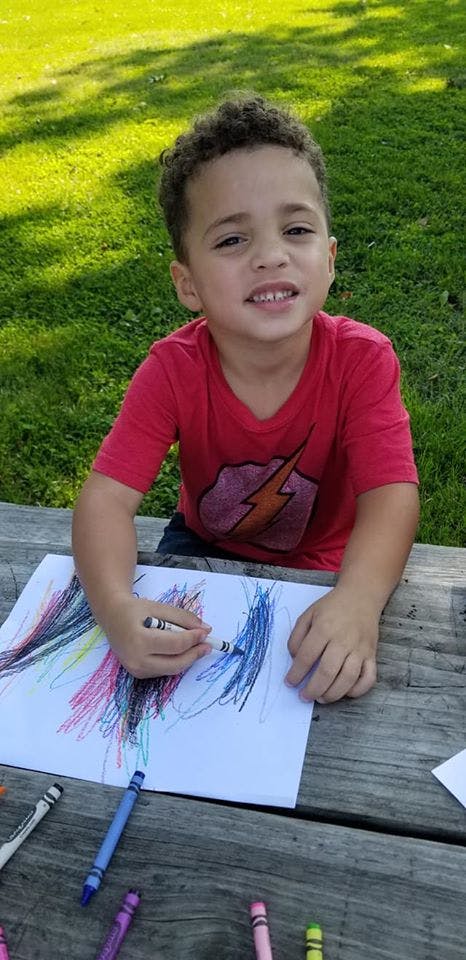 Child coloring on paper with crayons at a wooden table
