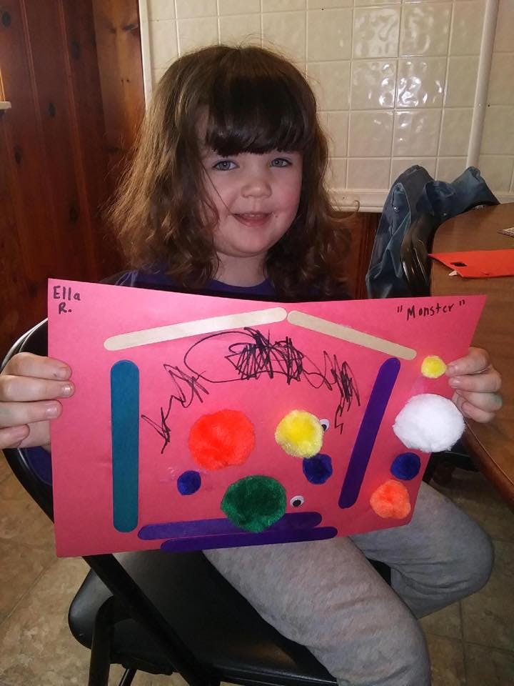 Child holding up a pink paper craft with pom-poms and craft sticks