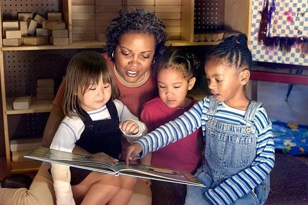 Adult and three children reading a book together