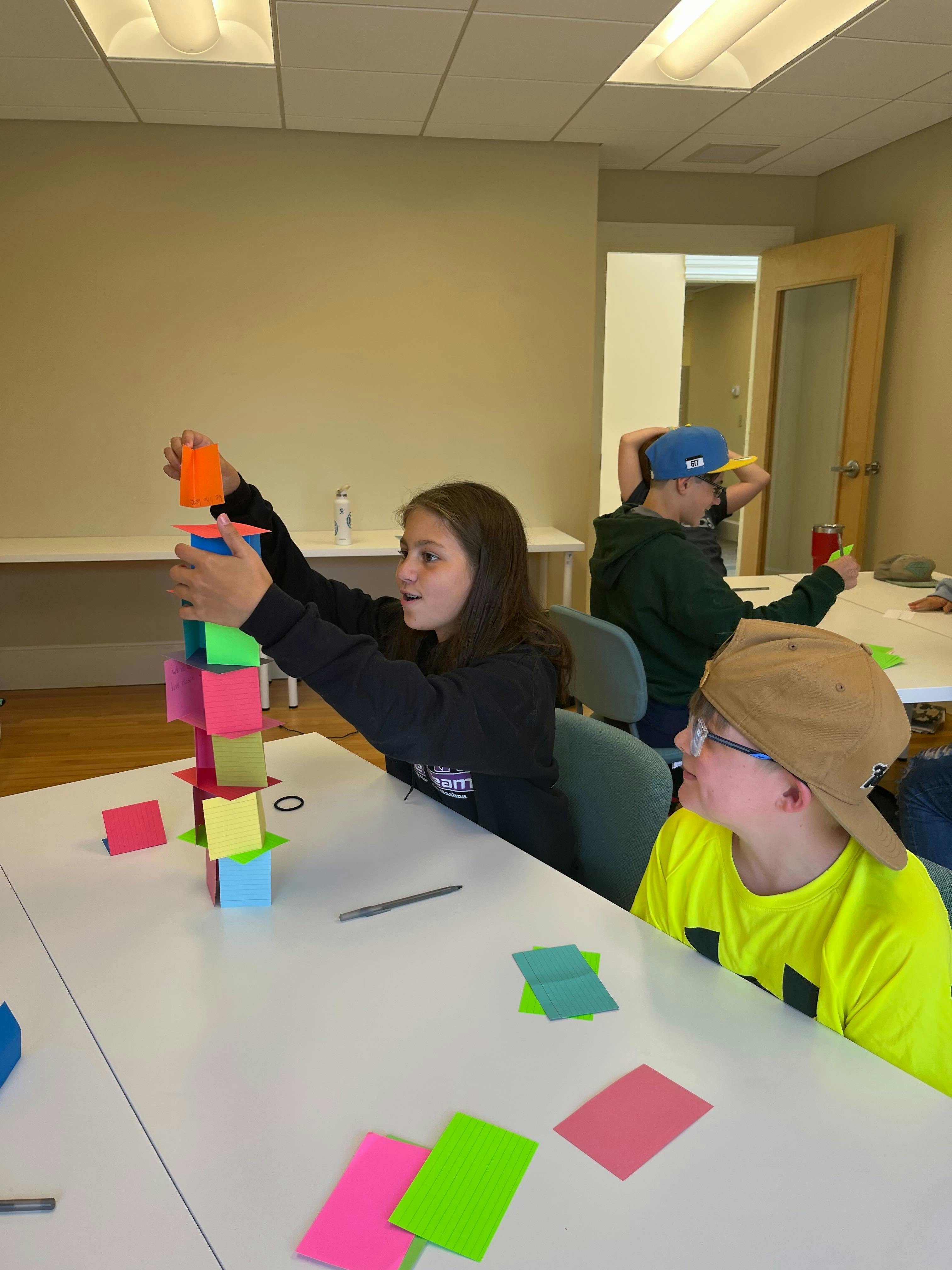 Teen building a tower of colorful blocks while another child watches