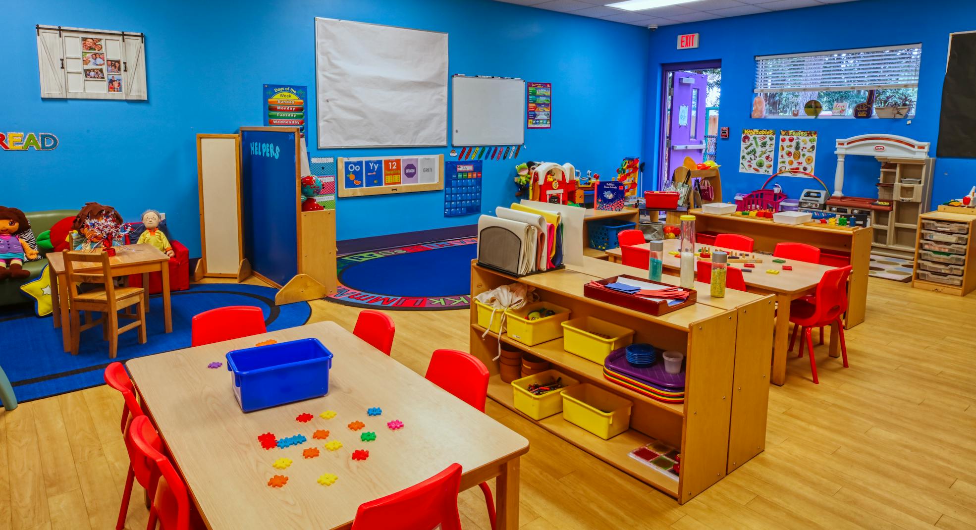 Classroom with child-sized tables and chairs, shelves with toys, and blue walls