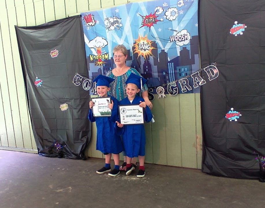 Person with two children in blue graduation caps and gowns holding certificates