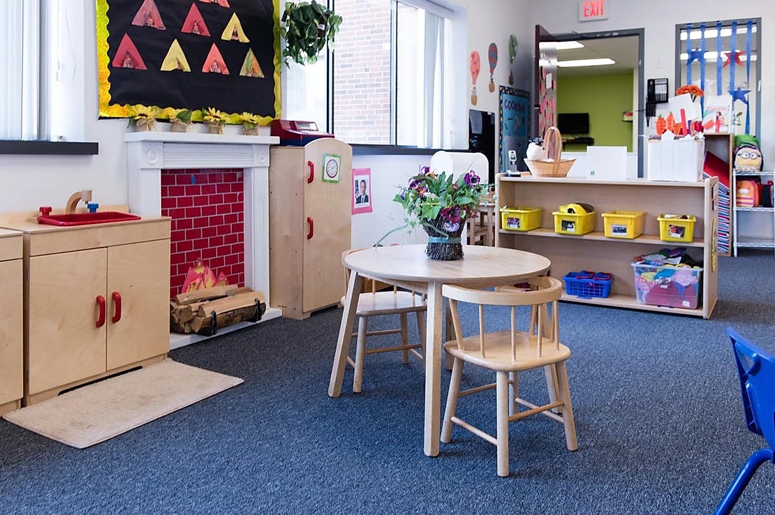 Classroom with small table and chairs, play kitchen, and shelves with a faux fireplace