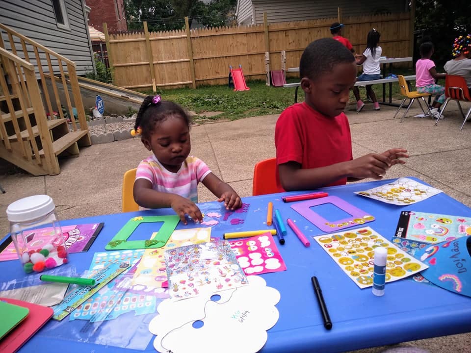 Two children sitting at a table doing crafts outdoors
