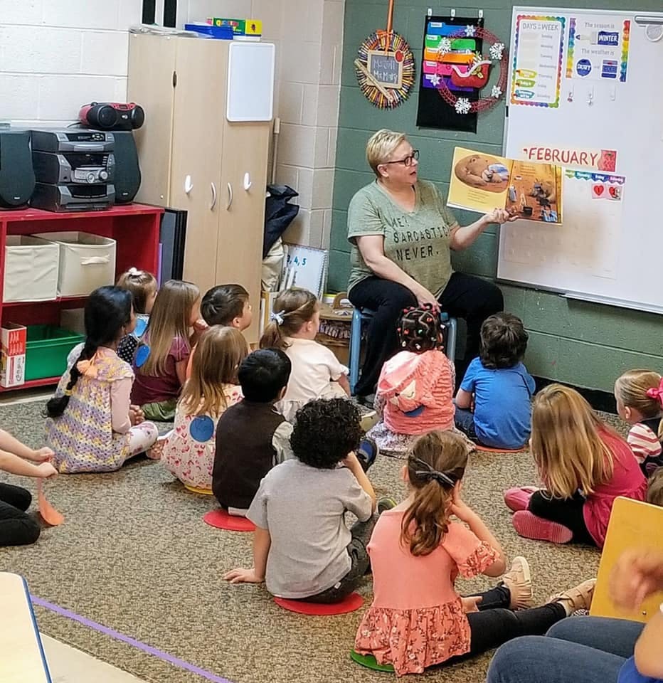 Person reading a book to a group of children in a classroom