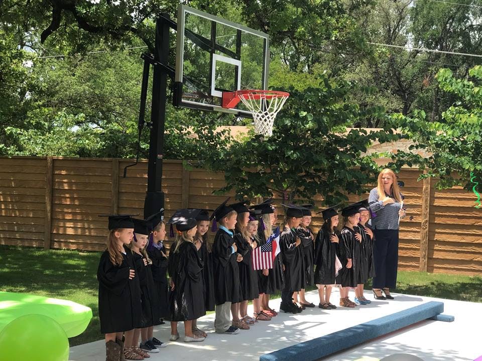 Adult and children in graduation caps and gowns standing in a line outdoors