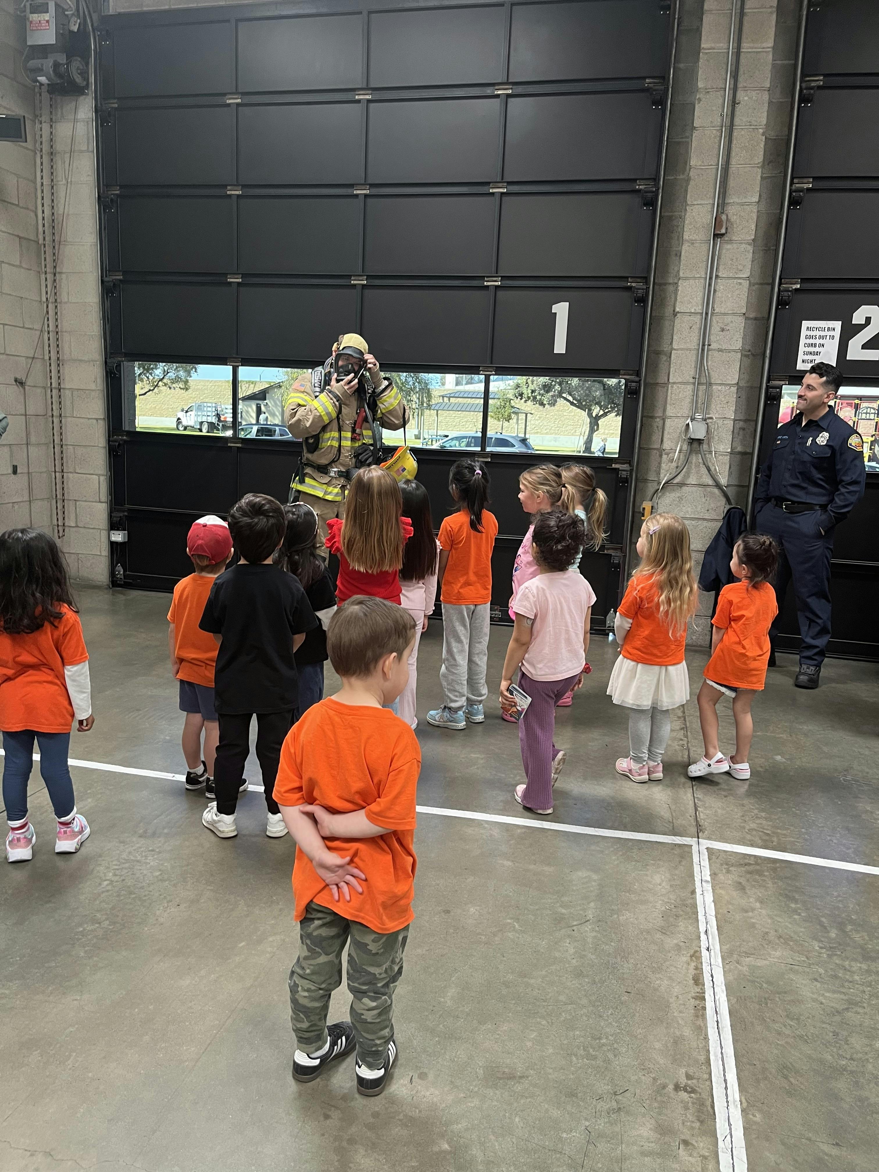 Group of children watching a firefighter in protective gear inside a fire station