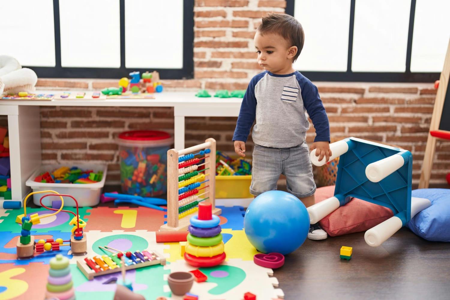 A young child standing near toys on a play mat in a room