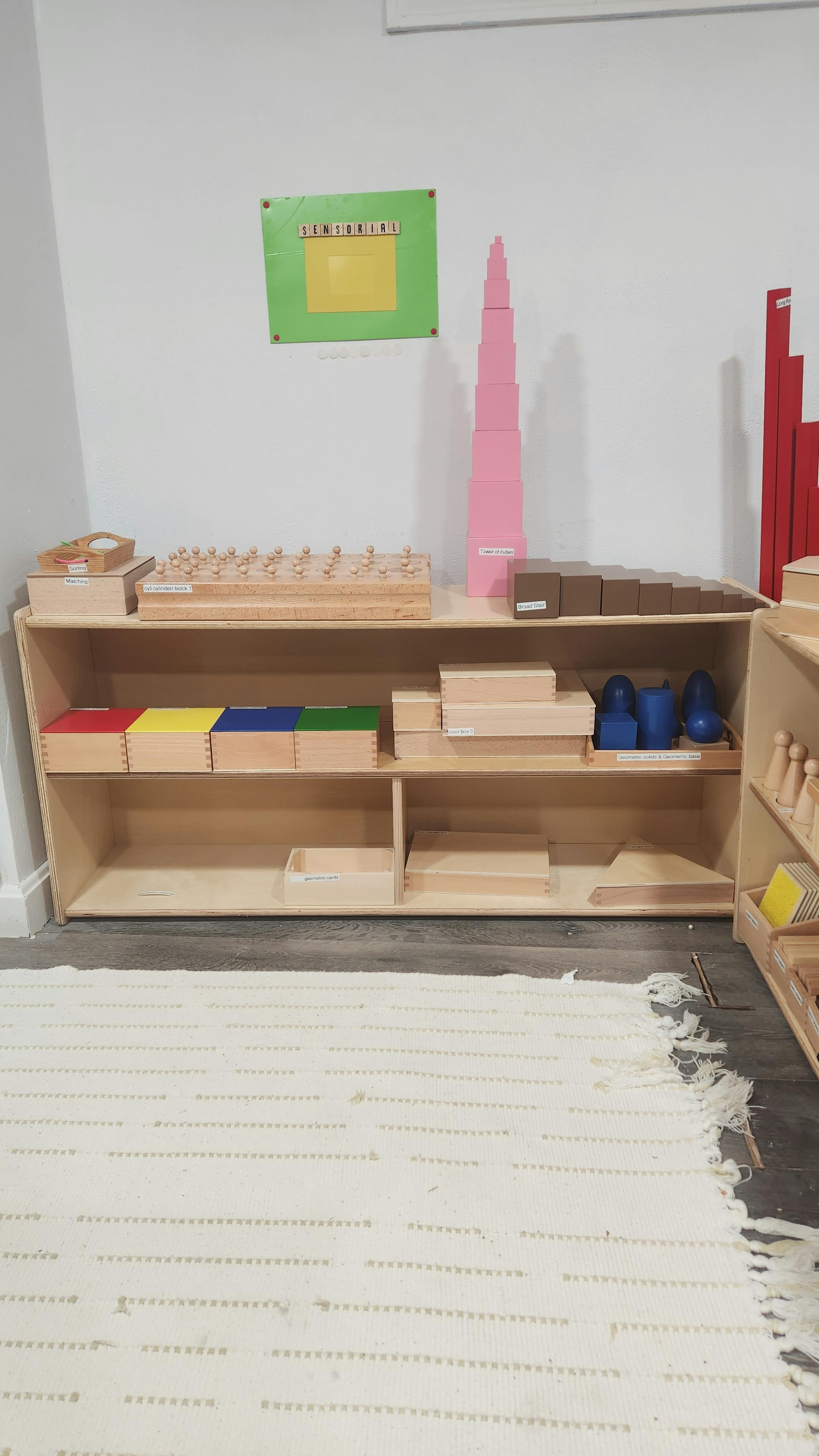 Wooden shelving unit with various educational materials and a pink tower
