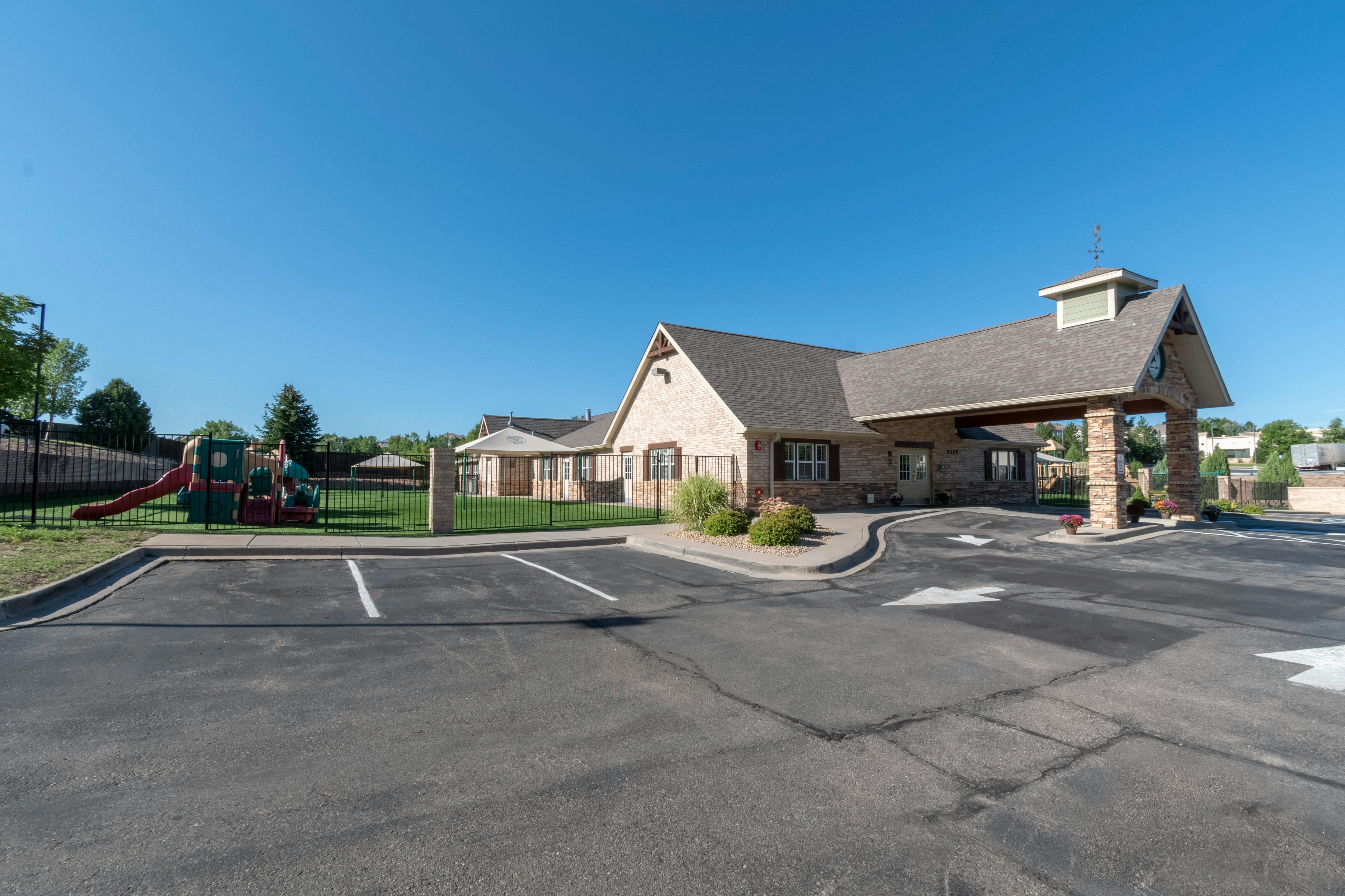 A beige building with a drive-through entrance, a fenced playground, and parking spaces