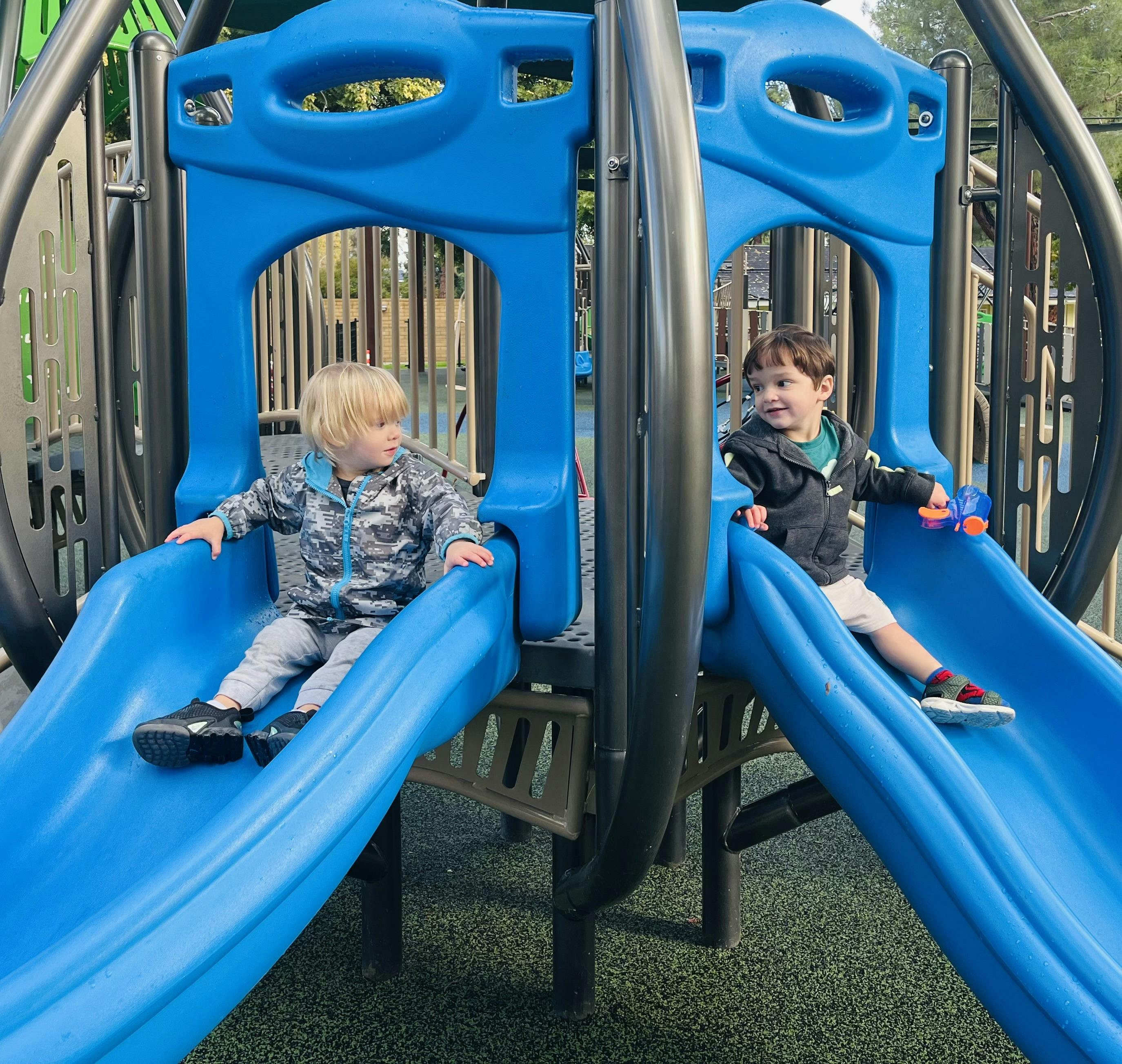 Two children sitting on blue slides on a playground
