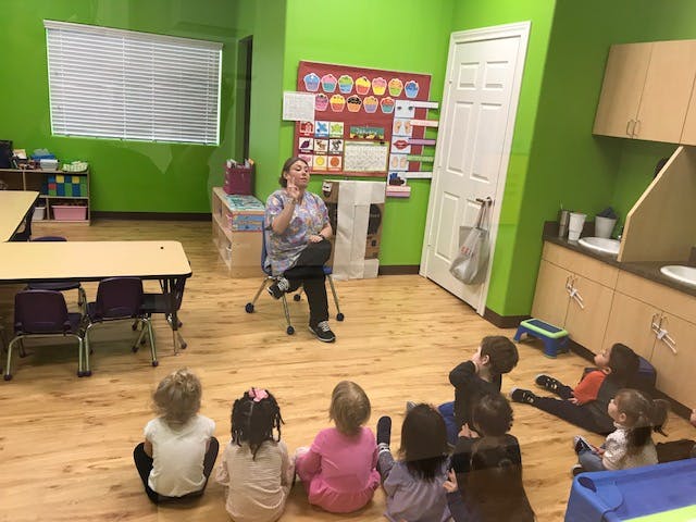 Adult speaking to a group of children sitting on the floor in a classroom
