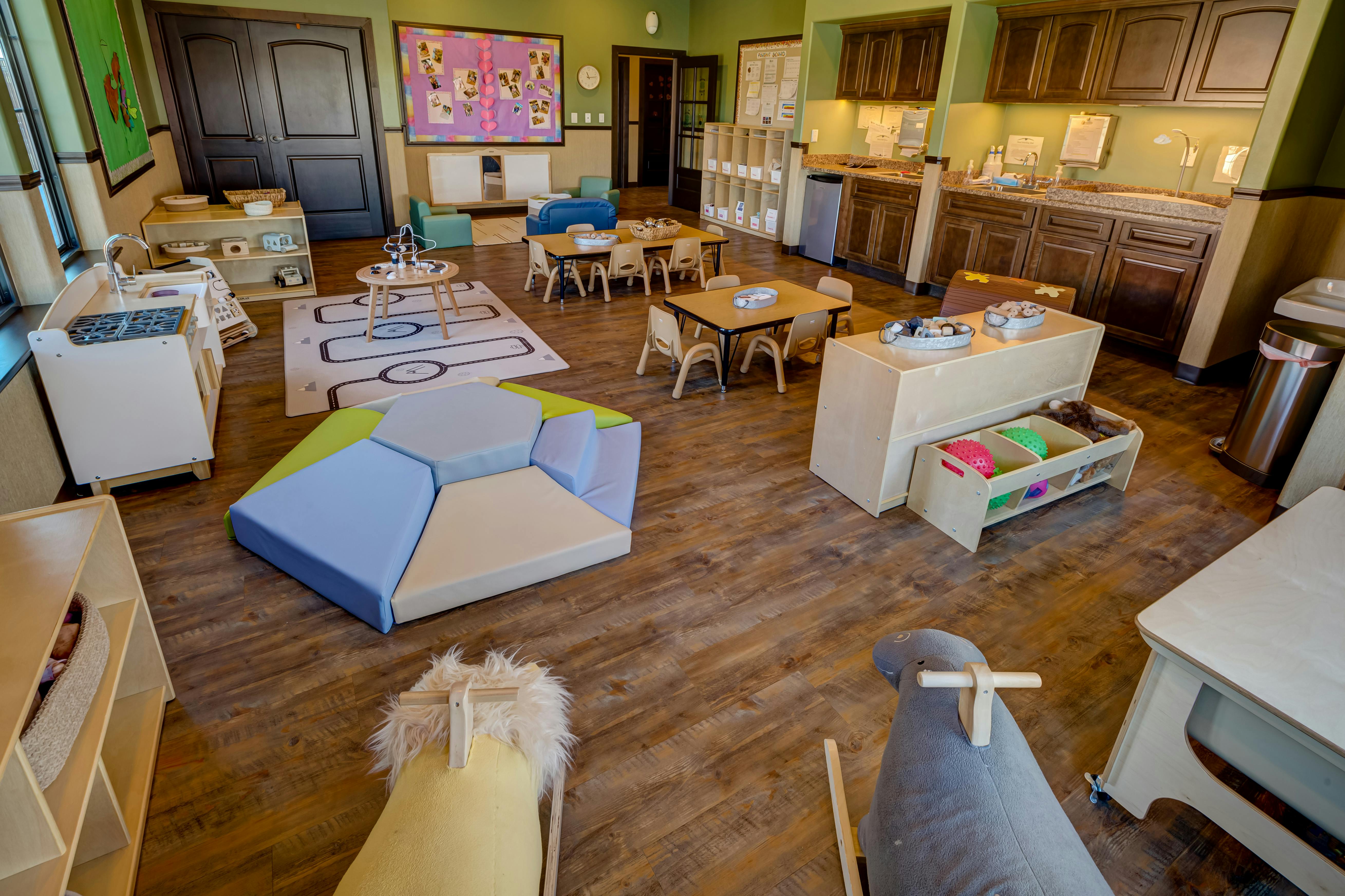 Playroom with small tables and chairs, soft play area, and kitchen counter