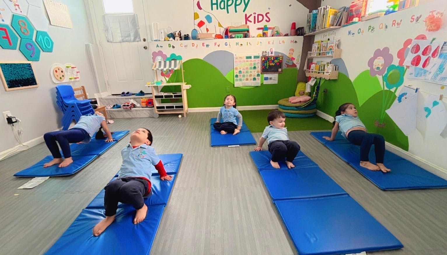 Children on blue mats in a classroom doing exercises