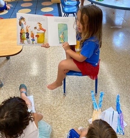 Child sitting on a small chair reading a book to other children