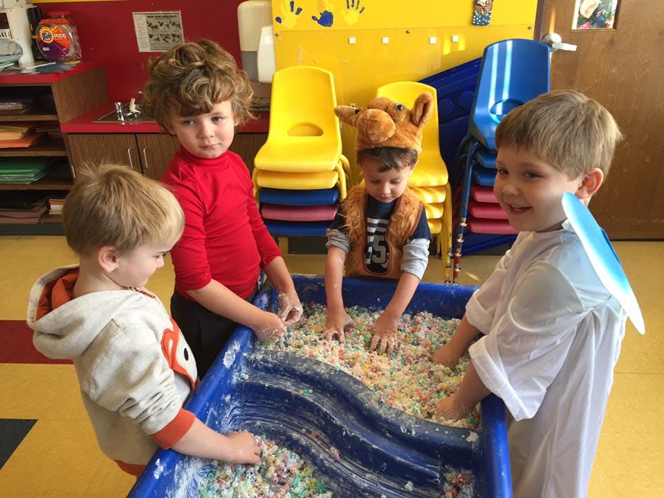 Four children playing in a sensory bin with colorful materials