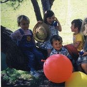 Children sitting on a tree branch with balloons