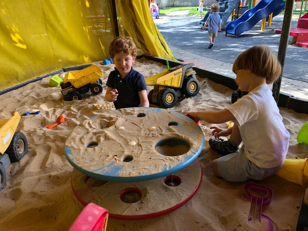 Two children playing in a sandbox with toy trucks