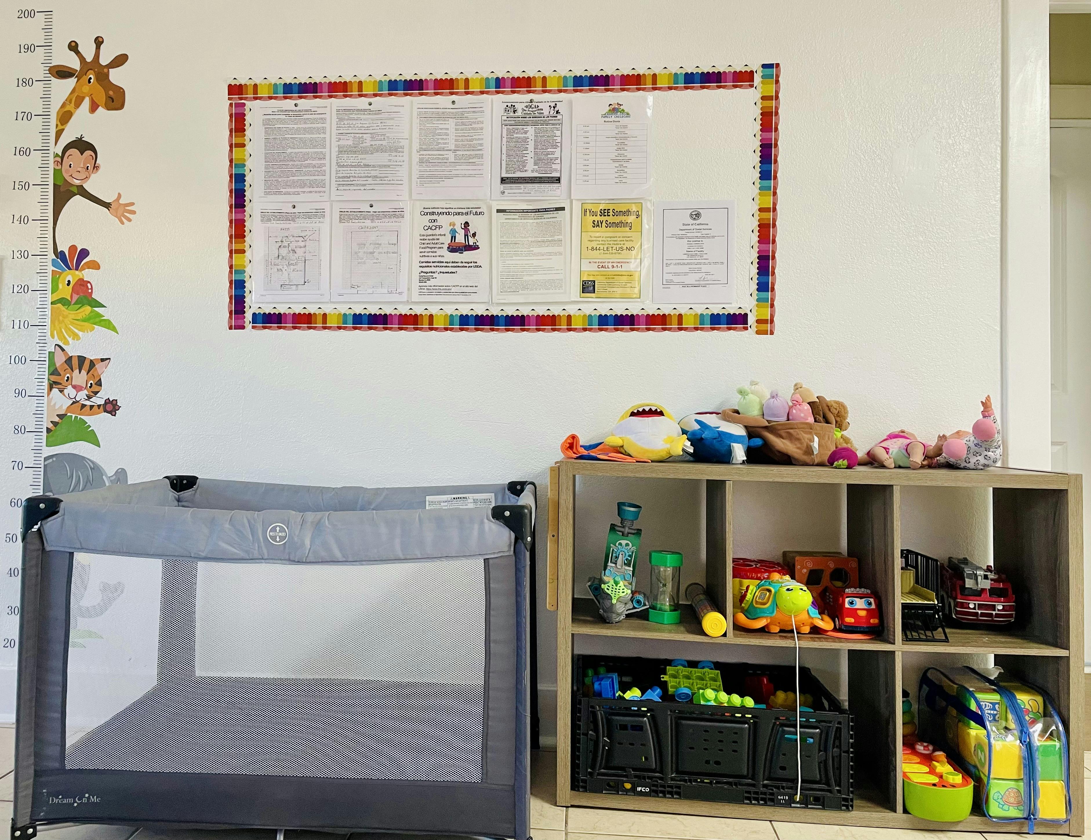Playpen next to a shelf with toys and a bulletin board on the wall