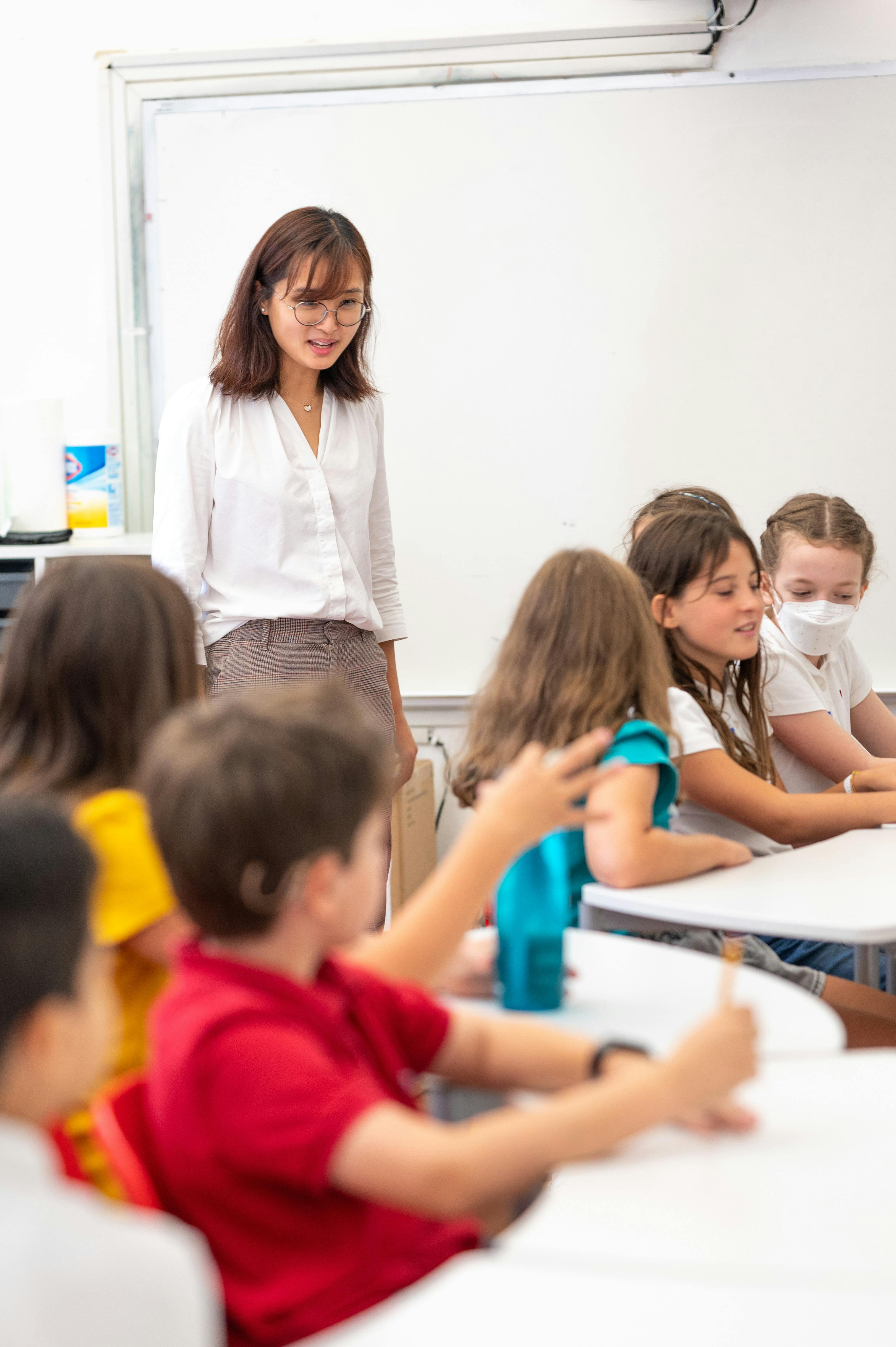 Person standing in front of children seated at desks in a classroom