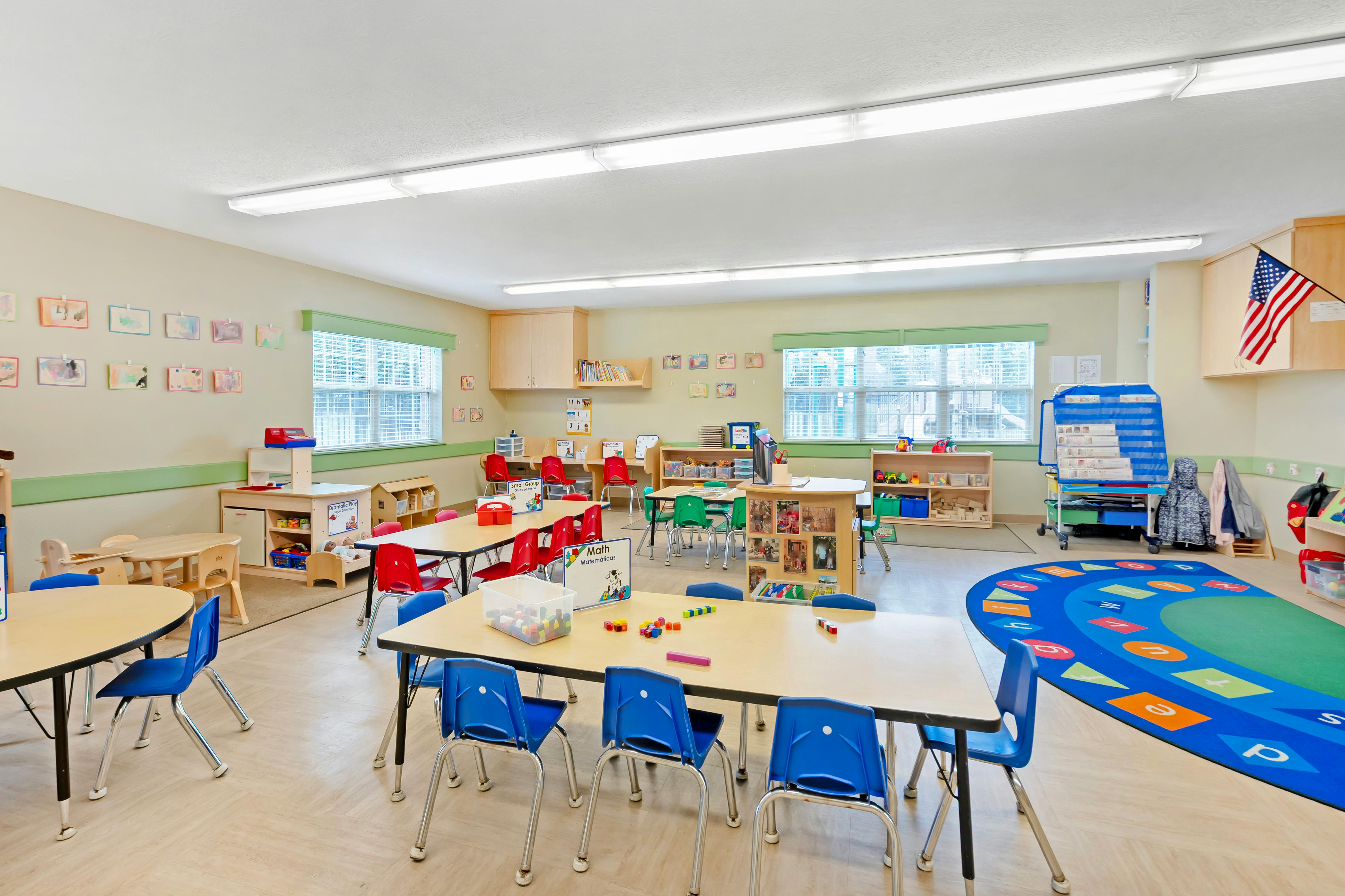 Classroom with child-sized tables and chairs, artwork on walls, and play areas