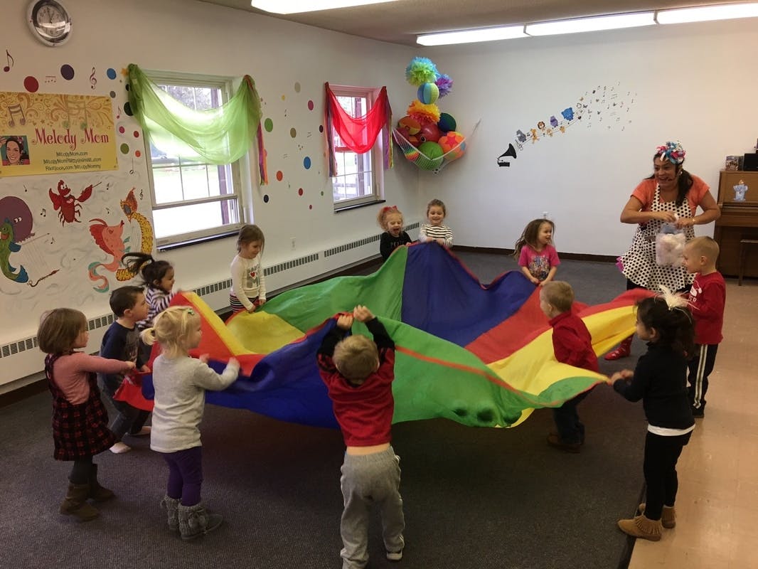 Children playing with a colorful parachute in a room with an adult