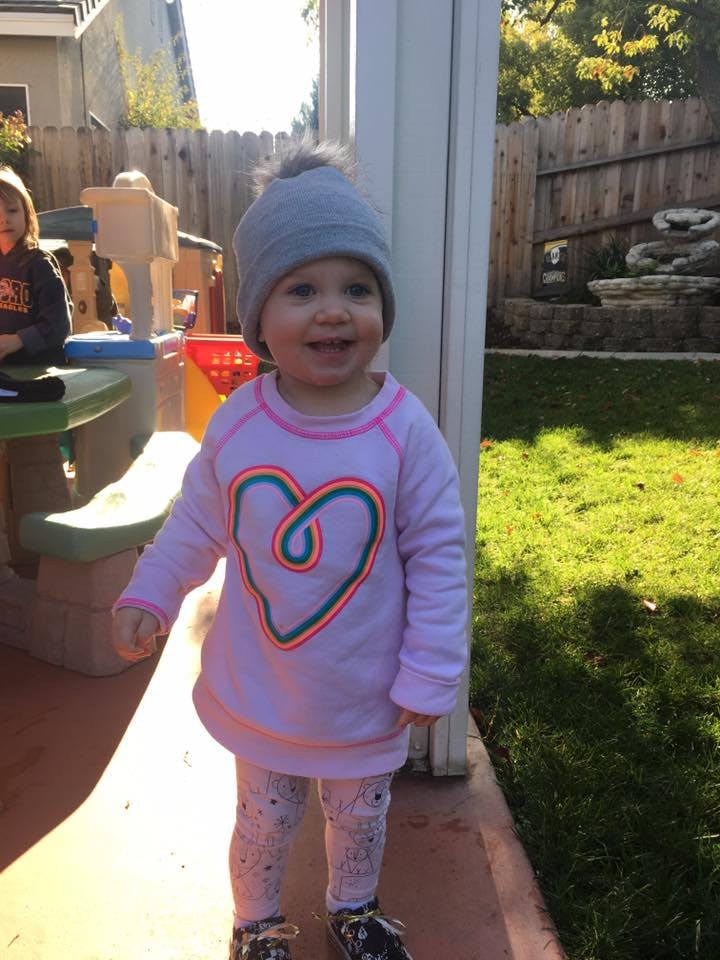 Child in a gray hat and pink shirt with a heart design standing outdoors