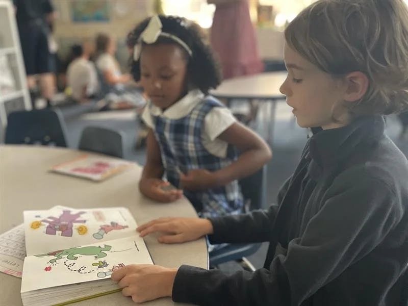 Child reading a book with another child in the background in a classroom