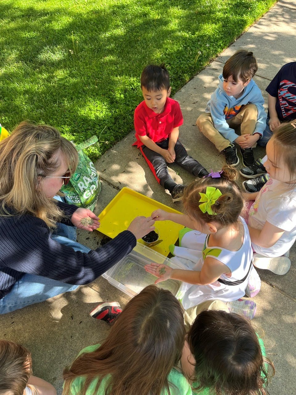 Adult and children on ground looking at items in a yellow tray