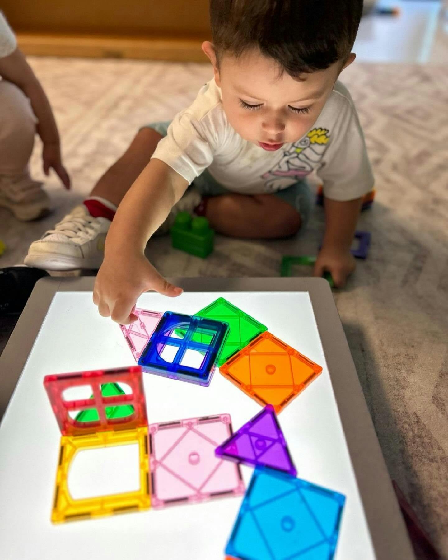 Child playing with colorful magnetic tiles on a light table