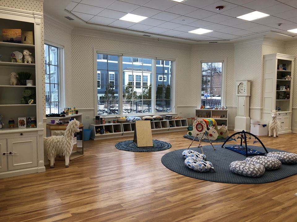 Playroom with wooden floors, large windows, and various play mats and seating areas