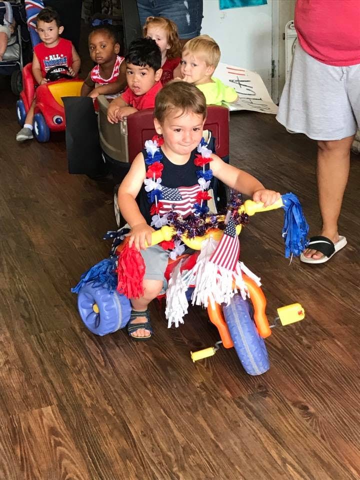Child on a decorated tricycle with other children in toy cars behind